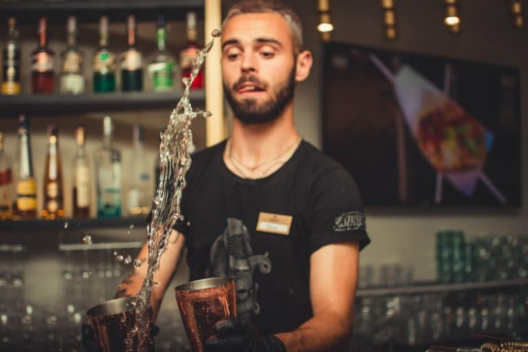 Bartender making a fancy drink with the liquid flying in the air. He is also sticking is tongue out a bit to concentrate.