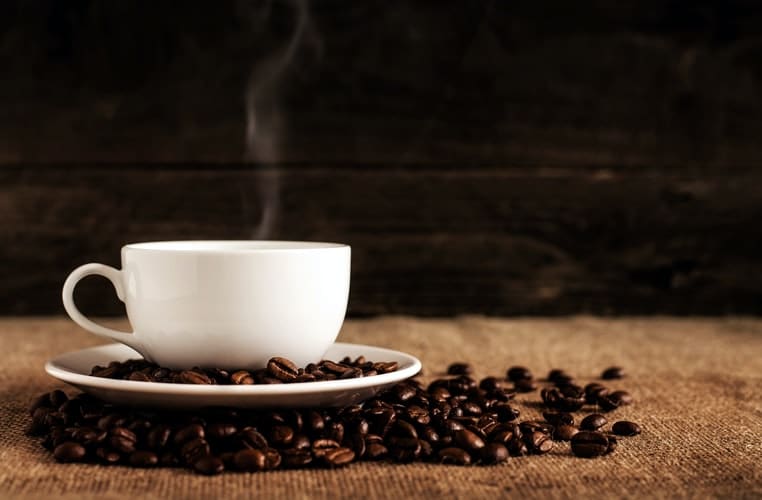 A cup of coffee surrounded by coffee beans.